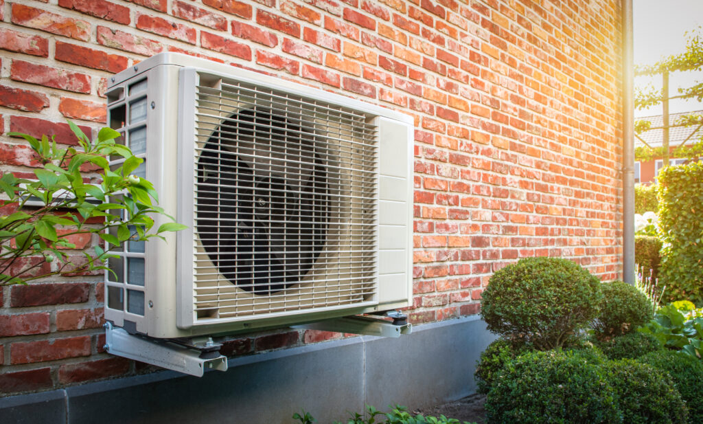 Side view of outdoor HVAC unit hanging on brick wall of house on a sunny day. 